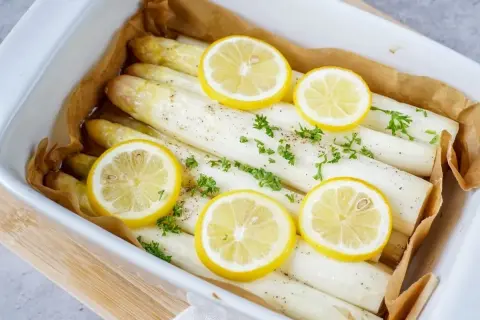 Frischer weißer Spargel, bereit zum Spargel kochen, garniert mit Zitronenscheiben und Petersilie in einer Auflaufform.
