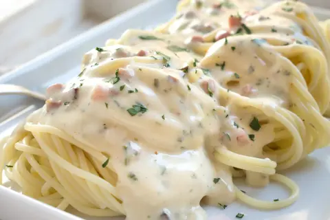 Cremige Spaghetti Carbonara mit Speckwürfeln und Petersilie, serviert auf einem weißen Teller.