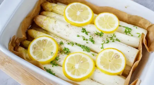 Frischer weißer Spargel, bereit zum Spargel kochen, garniert mit Zitronenscheiben und Petersilie in einer Auflaufform.