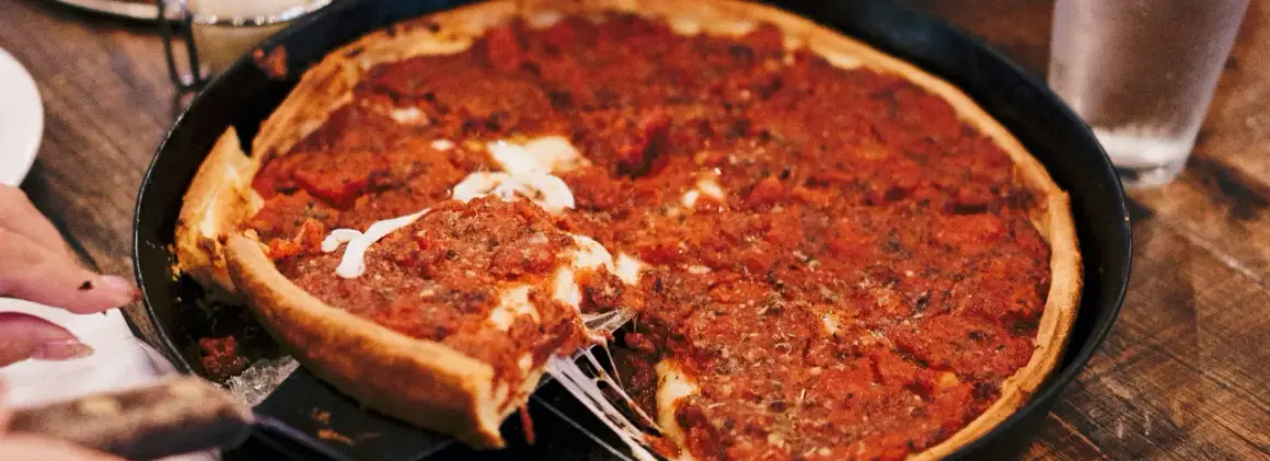 Ein Stück einer tiefen Chicago Style Pizza mit geschmolzenem Käse wird herausgehoben.