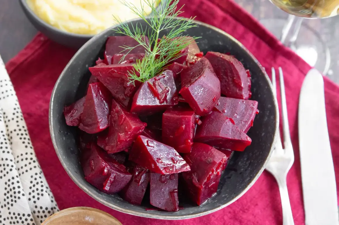 Schüssel mit gewürfelten, glänzenden roten Rüben, die man roh essen kann, garniert mit Dill. Daneben Kartoffelpüree und Besteck.