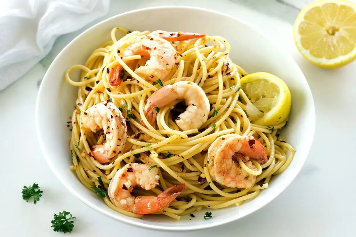 Ein Teller mit k&ouml;stlichen Spaghetti mit Garnelen, garniert mit Petersilie und Zitronenspalten.
