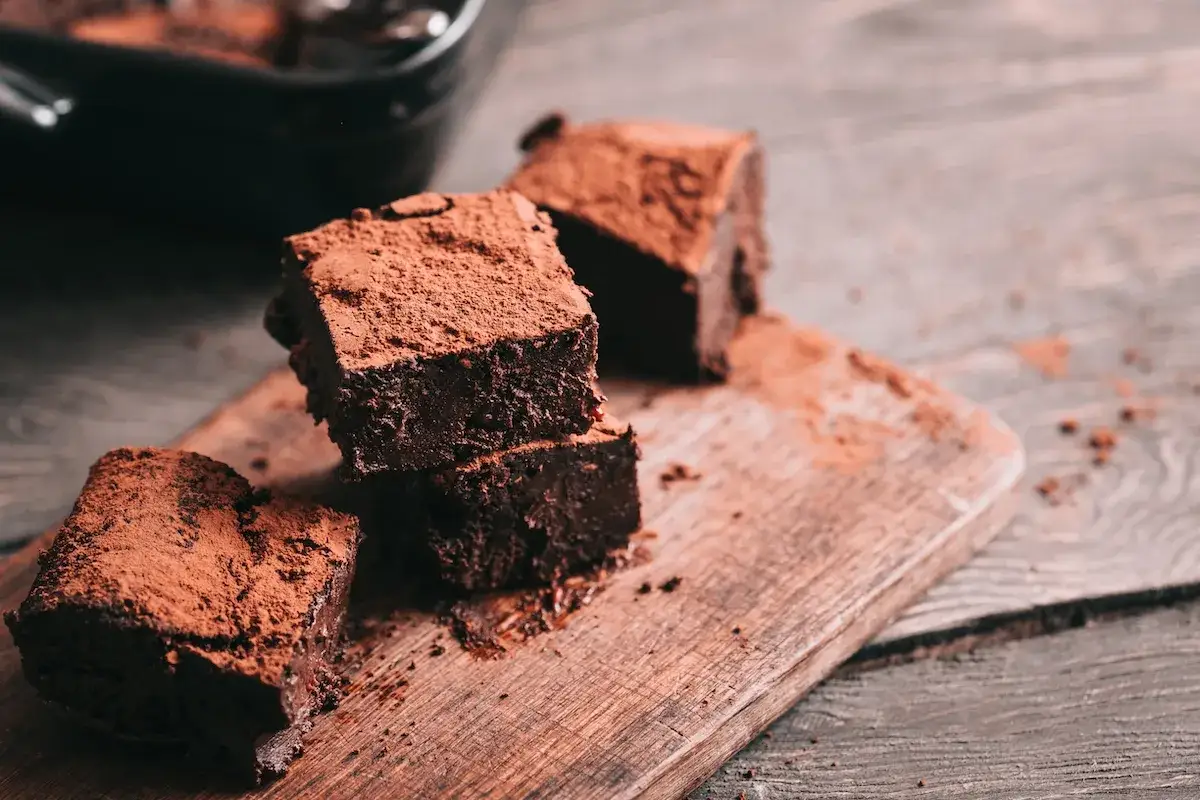Saftige Schokoladen-Brownies, bestäubt mit Kakaopulver, auf einem Holzbrett. Ein köstliches brownie rezept zum Nachbacken.