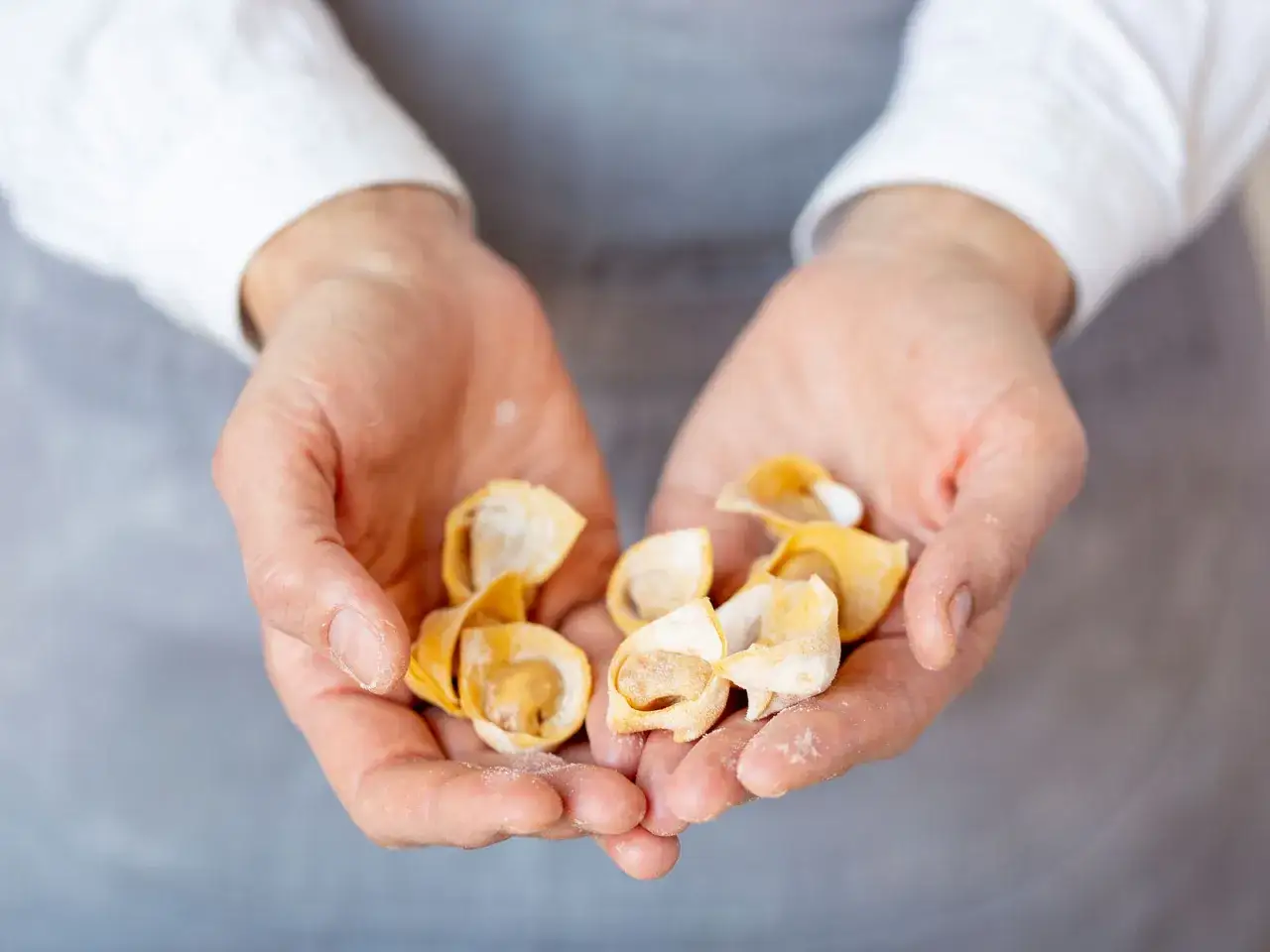 H&auml;nde halten frisch gemachte, kleine Tortellini. Das Ergebnis von liebevollem Tortellini selber machen.