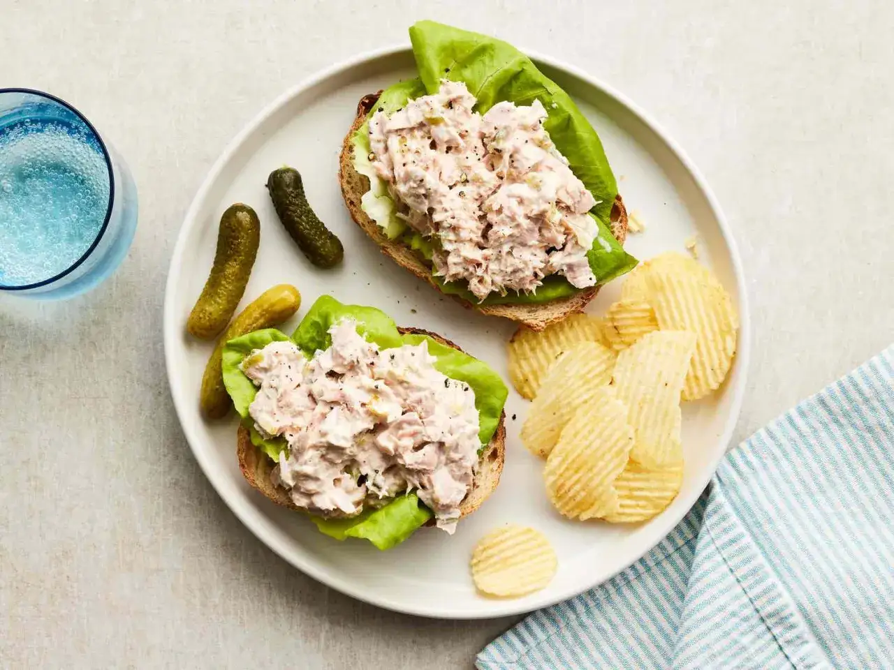 Zwei offene Sandwiches mit Thunfischsalat auf Salatblatt und Vollkornbrot, dazu Cornichons und Kartoffelchips. Perfekt für schnelle Thunfisch Rezepte.