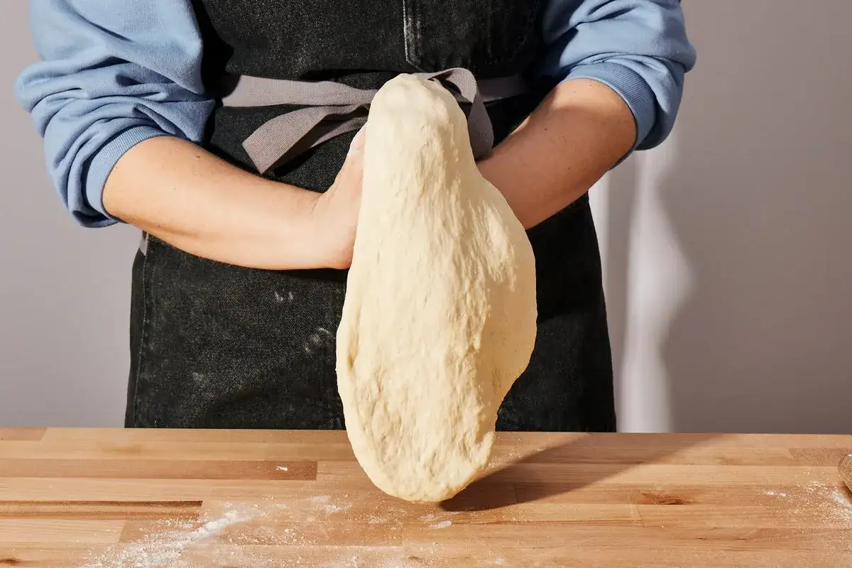 Hände formen einen elastischen Pizzateig. Das Rezept für perfekten Teig ist hier.