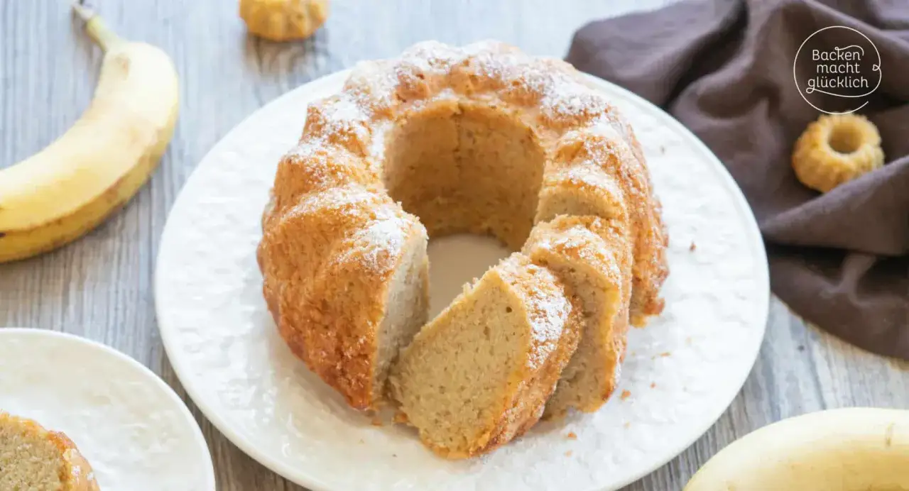 Reife Bananen verwerten: Ein saftiger Bananenkuchen mit Puderzucker best&auml;ubt, daneben eine Banane und ein kleines Gugelhupf-F&ouml;rmchen.