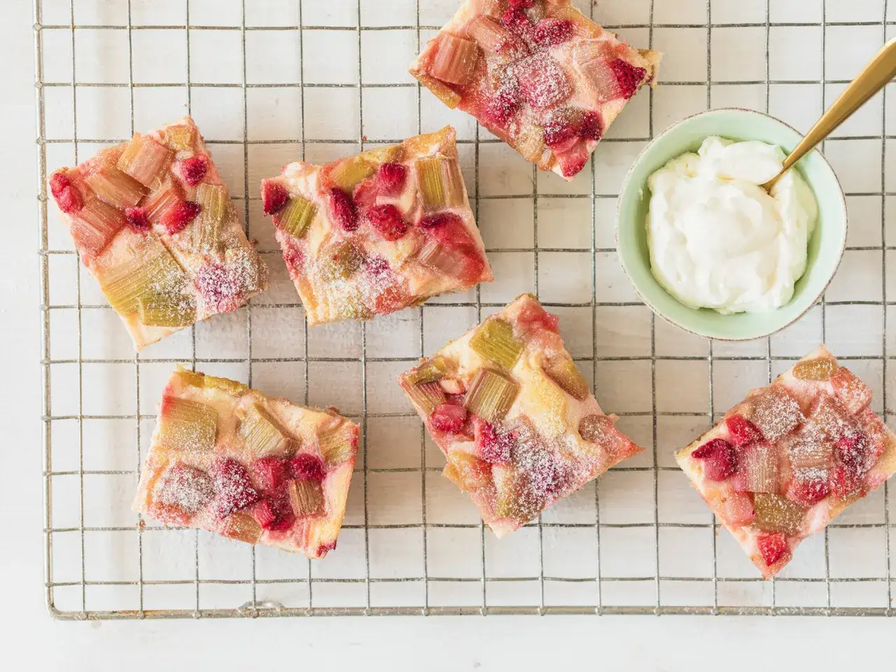 Saftiger Erdbeer Rhabarber Kuchen, bestäubt mit Puderzucker, wartet neben einer Schüssel Schlagsahne auf seine Liebhaber.