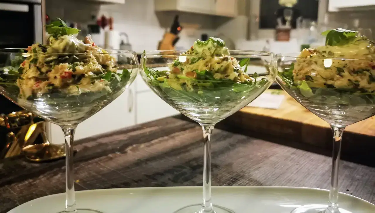 Drei Gl&auml;ser mit einem leckeren Krabbencocktail mit Avocado und frischen Kr&auml;utern, serviert auf einem Bett aus Rucola.