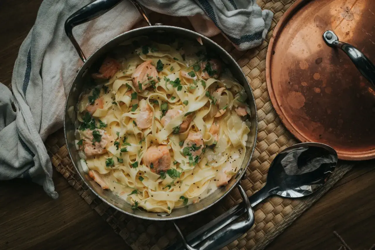 Tagliatelle al salmone in cremiger Sauce, garniert mit frischer Petersilie und schwarzem Pfeffer. Ein k&ouml;stliches Gericht, das zum Genie&szlig;en einl&auml;dt.