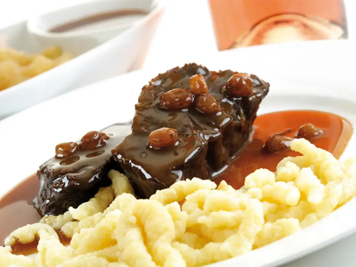 Zwei Stücke zarter Sauerbraten mit Rosinen in dunkler Sauce, serviert mit Spätzle. Ein köstliches Sauerbraten Rezept.