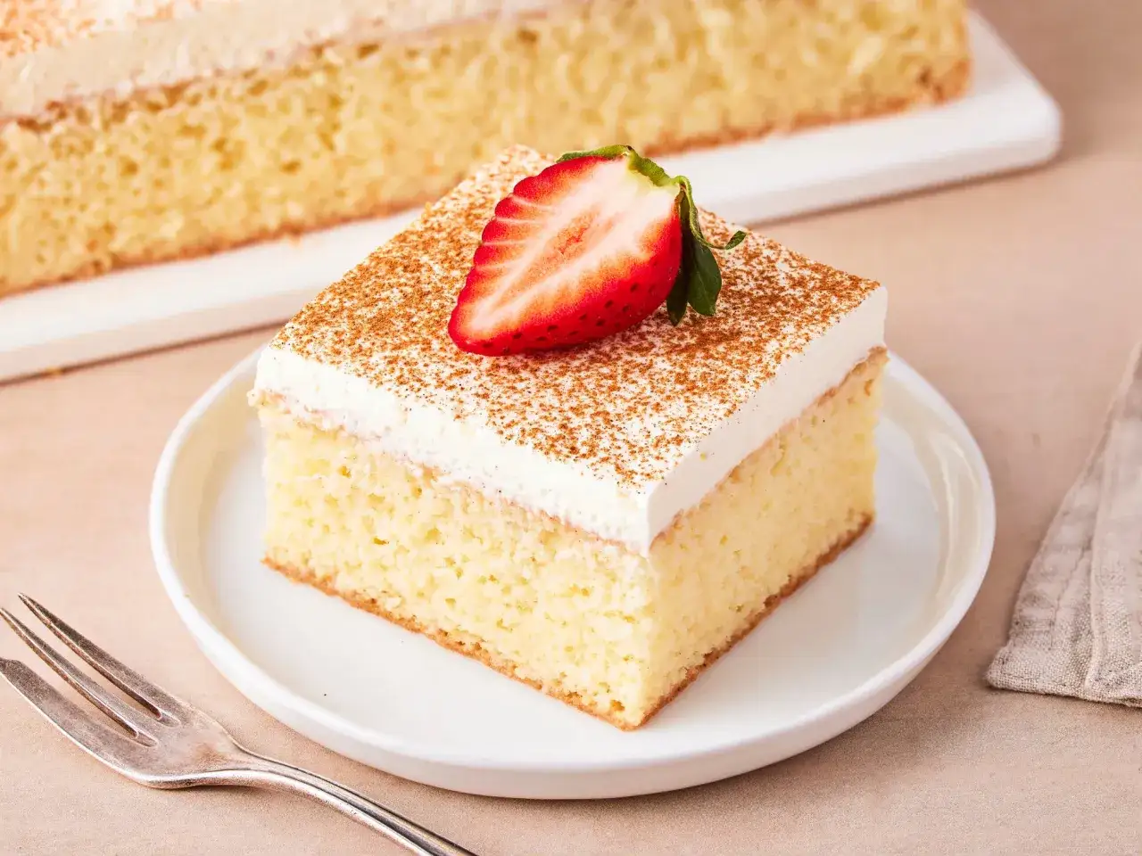 Ein St&uuml;ck saftiger Tres Leches Kuchen, garniert mit einer Erdbeerh&auml;lfte und Zimt.