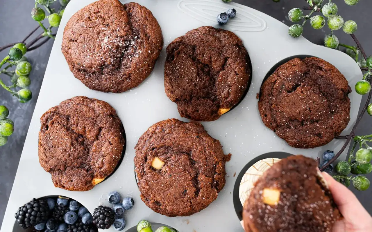 Schokomuffins rezept: Saftige Schokomuffins mit wei&szlig;en Schokost&uuml;ckchen in einer Muffinform, garniert mit Beeren und gr&uuml;nen Beeren.