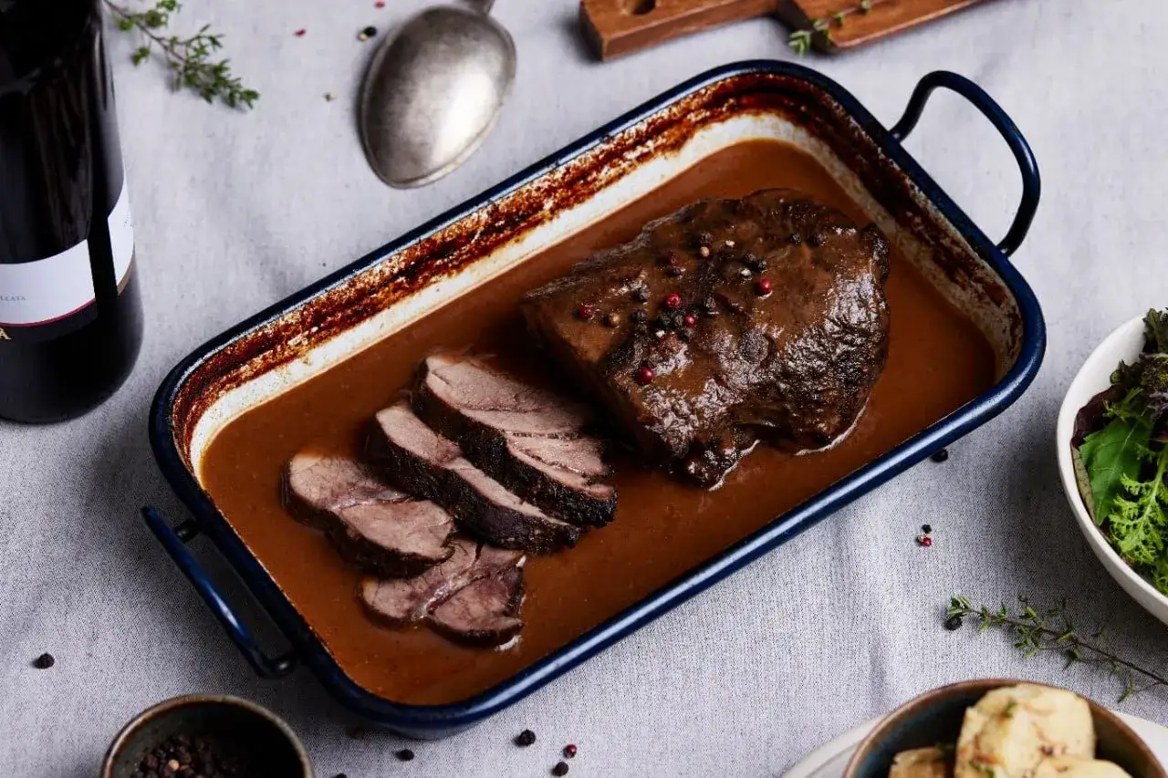 Ein k&ouml;stliches Rehschulter Rezept: zartes Fleisch in dunkler Sauce, garniert mit Pfefferk&ouml;rnern, serviert mit Beilagen.