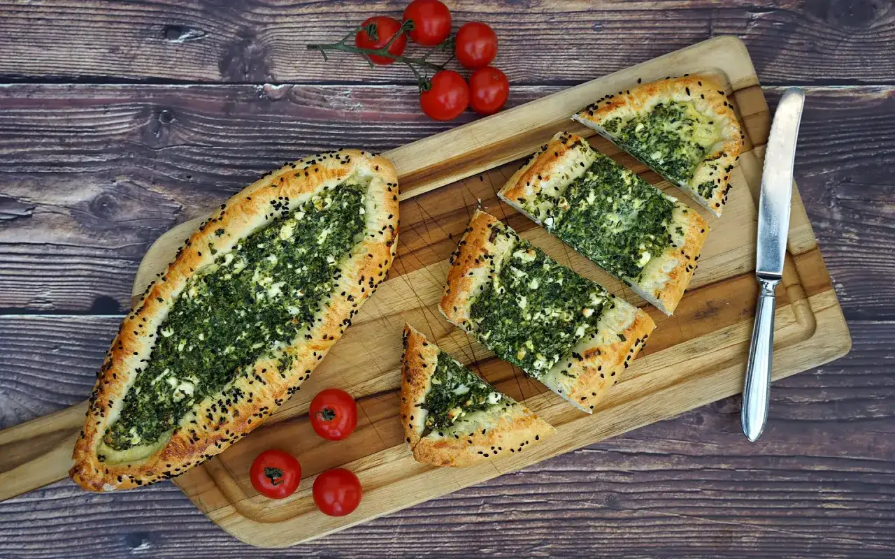 Ein leckeres Pide Rezept mit Spinat und Feta, garniert mit schwarzen Sesamkörnern. Daneben liegen frische Kirschtomaten.