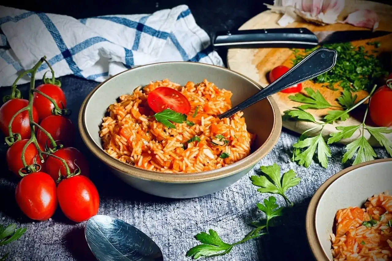 Sch&uuml;ssel mit aromatischem griechischem Reis, garniert mit Tomaten und Petersilie. Frische Tomaten und Knoblauch im Hintergrund.