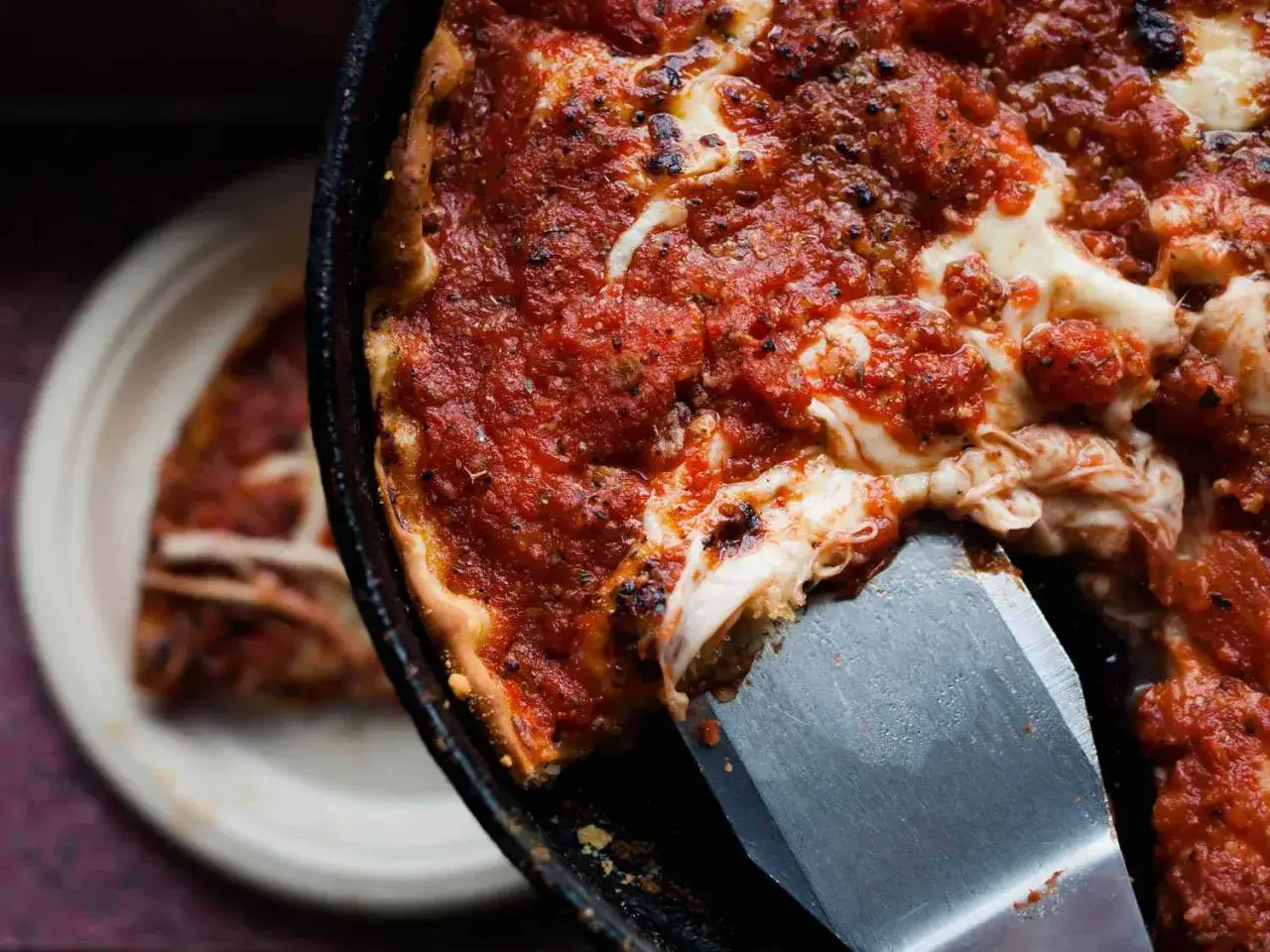 Ein St&uuml;ck einer tiefen, saftigen Chicago Style Pizza wird mit einem Spachtel herausgehoben. Der K&auml;se zieht F&auml;den.