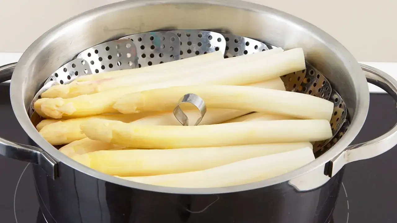 Frischer weißer Spargel liegt im Dampfkorb, bereit zum Spargel kochen. Ein kleiner Metallring hält die Stangen zusammen.
