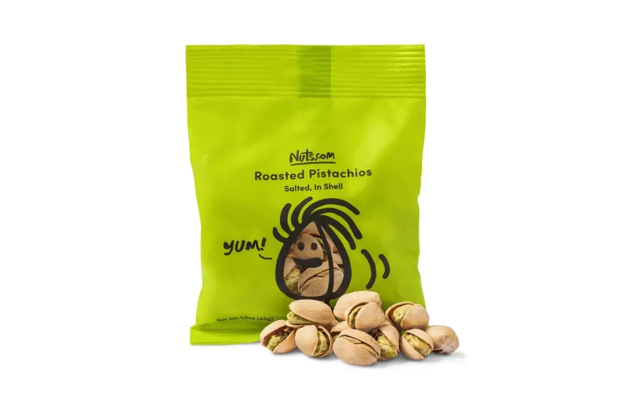 Gr&uuml;ne T&uuml;te mit ger&ouml;steten Pistazien von Nuts.com. Ein paar Pistazien liegen davor. Wie gesund sind Pistazien? Sie sind ein toller Snack!