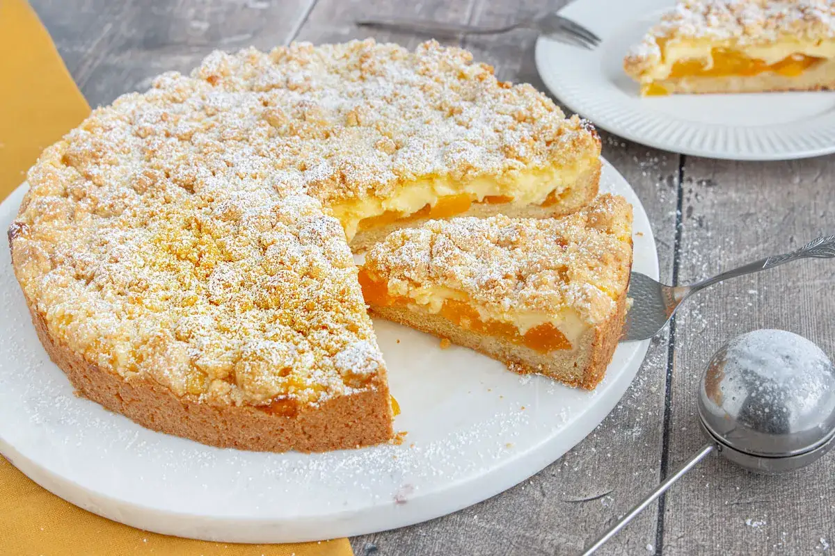 Ein saftiger aprikosenkuchen mit streusel, bestäubt mit Puderzucker. Ein Stück wird gerade serviert.