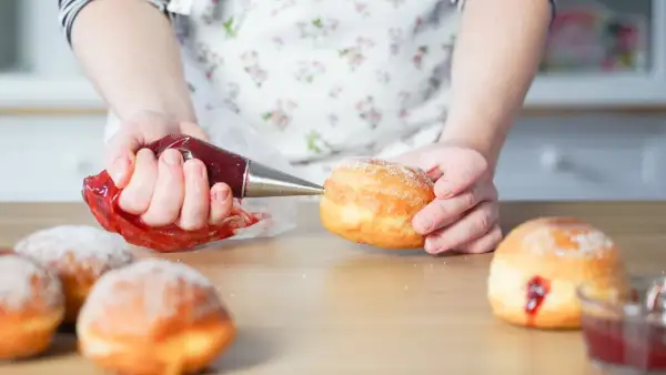 Hände füllen mit Marmelade gefüllte, zuckerbestäubte **bolas de fraile** mit einem Spritzbeutel.